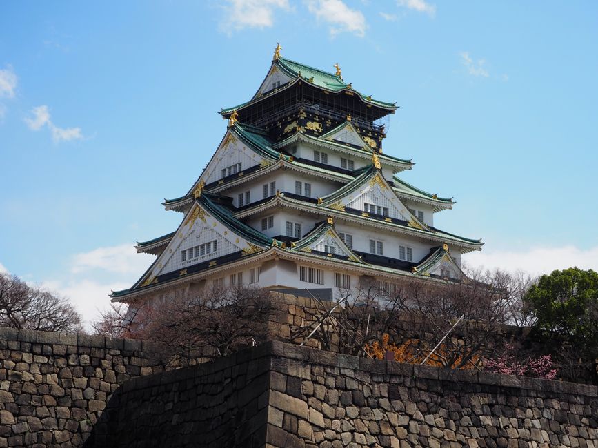 Historic Osaka Castle surrounded by spring foliage under a clear blue sky.